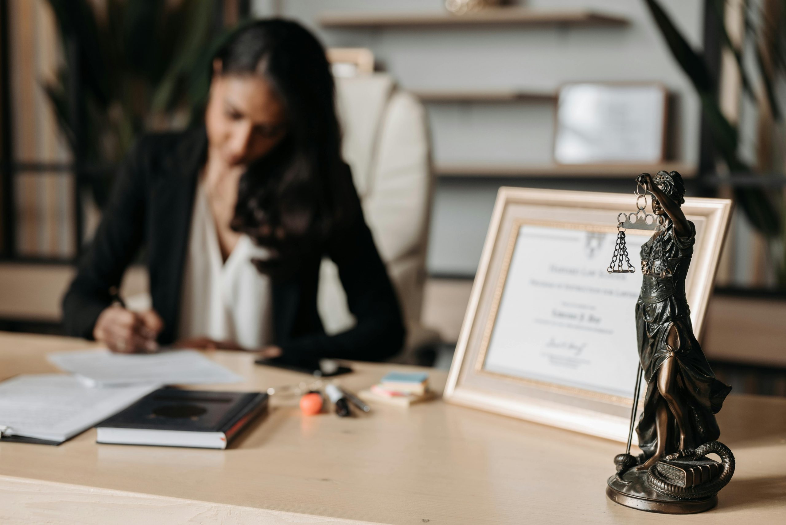attorney focused on work at her desk, with a framed certificate and a lady justice statue