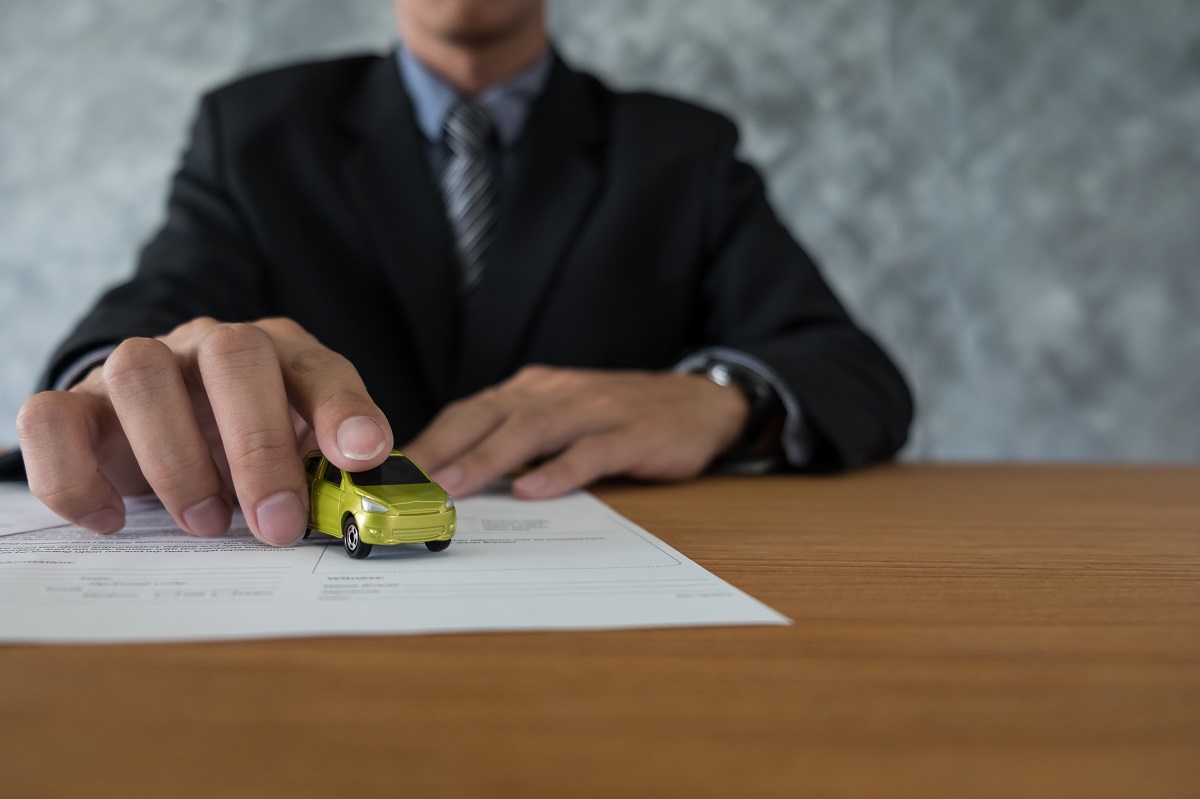 lawyer in a suit and tie holding a green toy car placed on top of a document